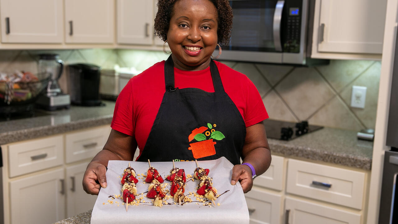 A woman holds a baking sheet of prepared Frozen Banana Splits