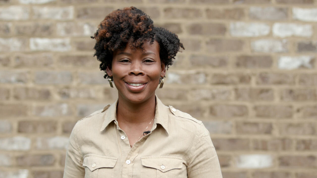 A woman stands in front of a brick wall.