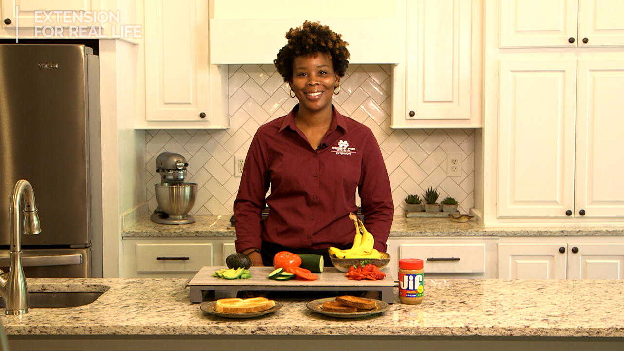 A woman stands behind a kitchen counter of breakfast toast and toppings.