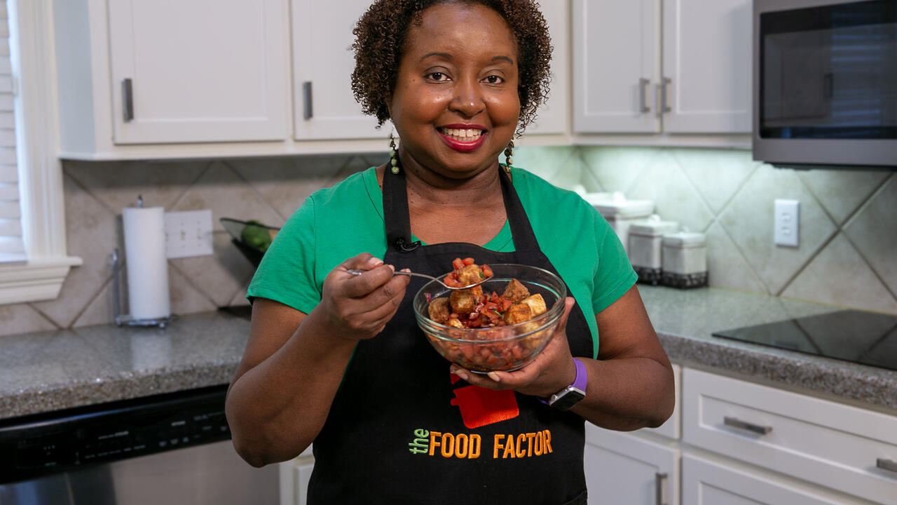 A woman in a kitchen holds a bowl of bruschetta salad.