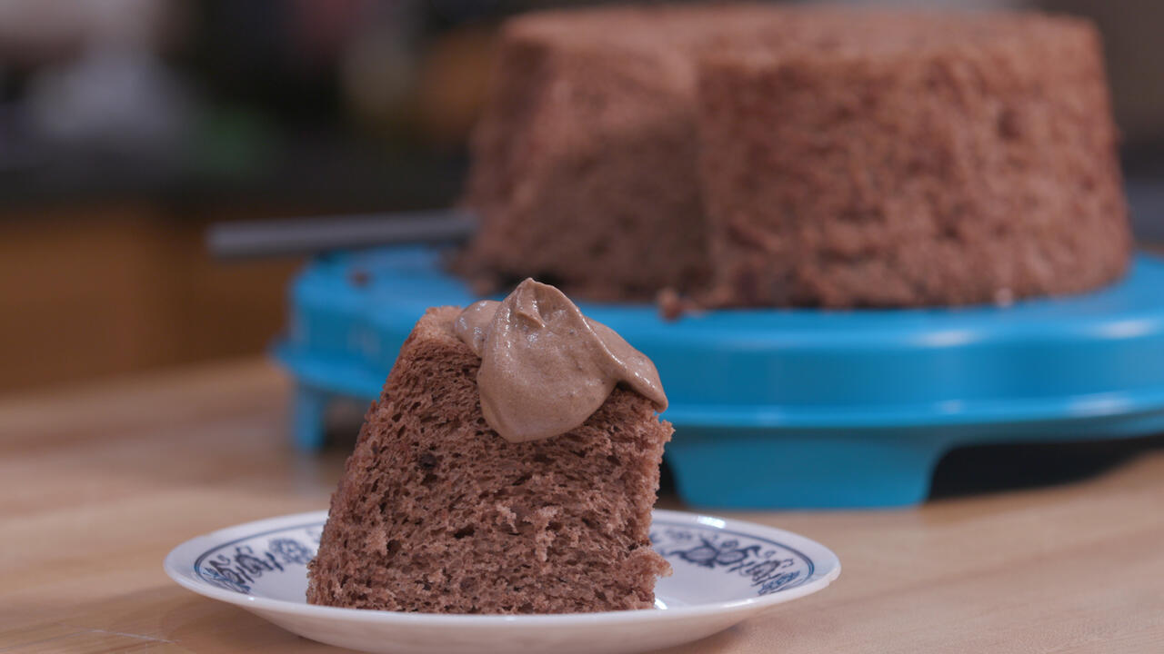 A slice of chocolate angel food cake on a small saucer with the entire cake on a blue platter in the background