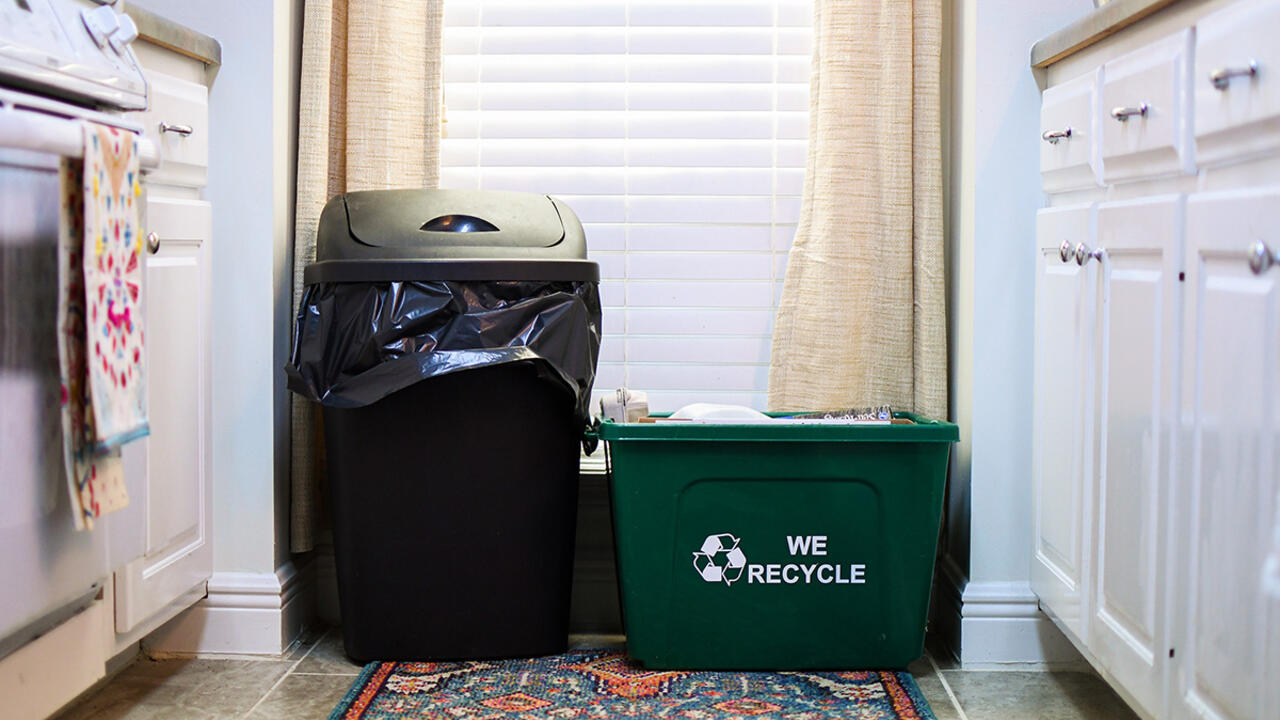 A green recycling bin sitting next to a black trashcan. 