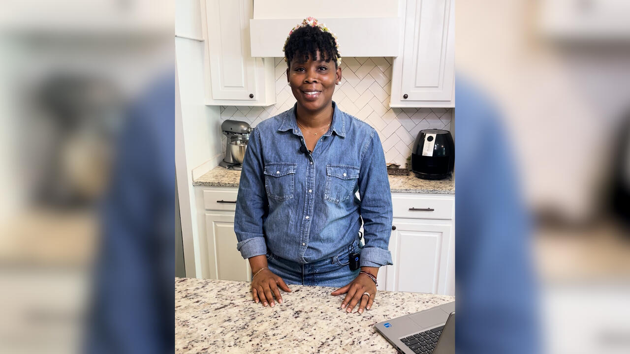 A woman standing at a kitchen counter smiles at the camera.