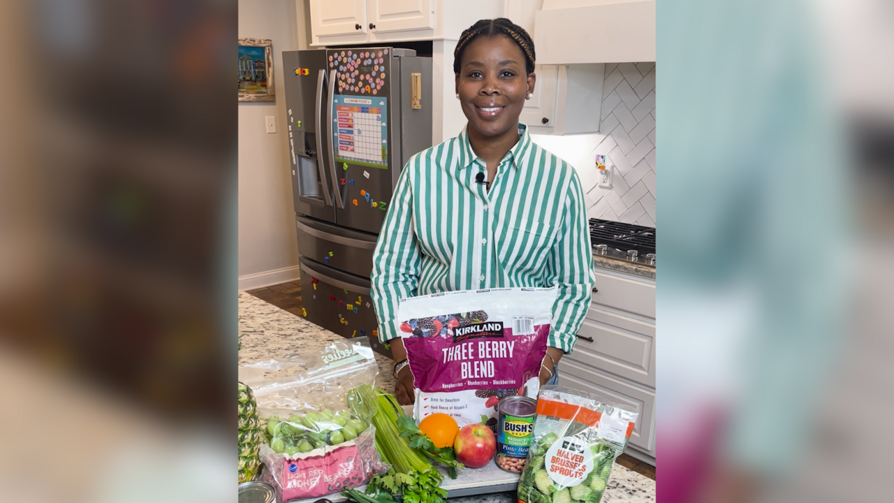 A woman stands behind a kitchen counter with a variety of foods displayed.