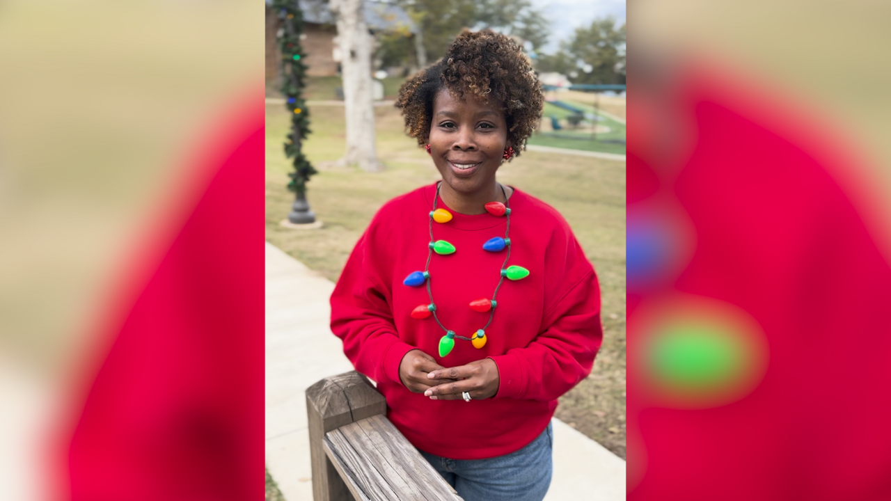 A woman stands on a sidewalk in a red sweatshirt and festive holiday-themed necklace.