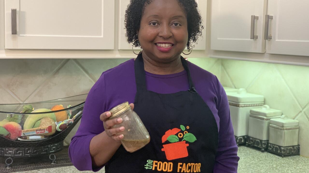 A woman stands in a kitchen and holds a jar of red wine vinaigrette.