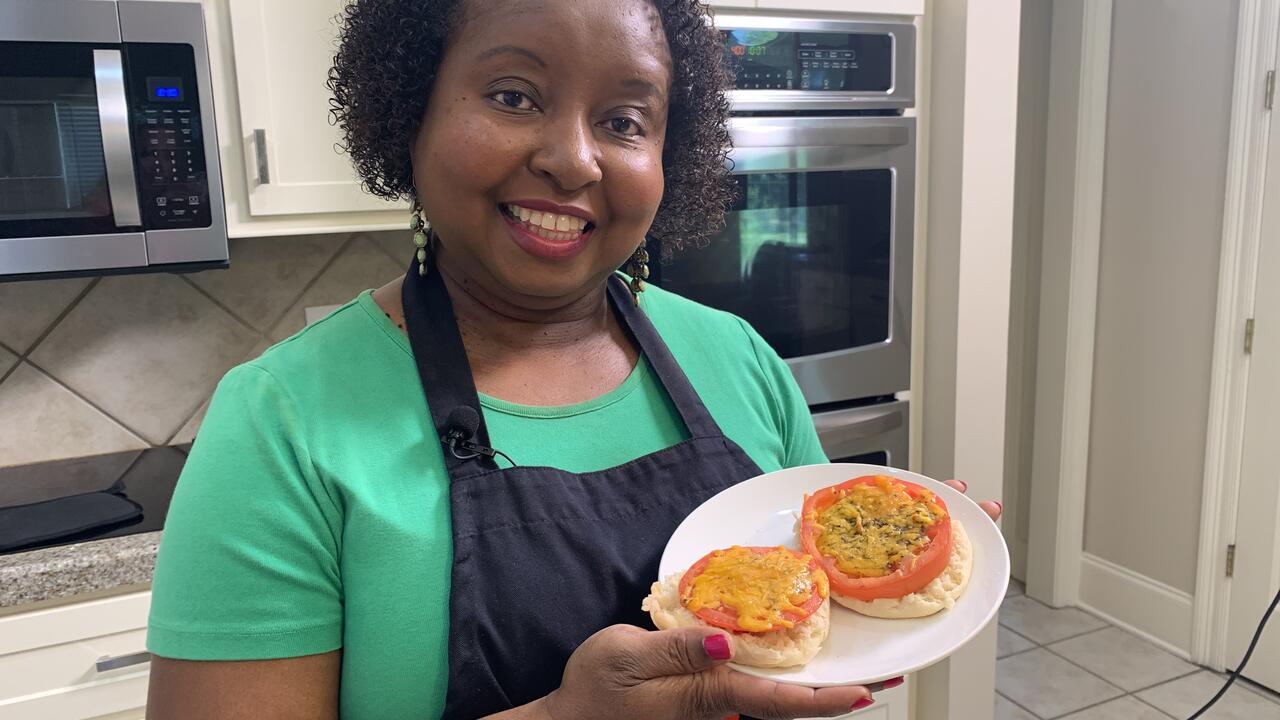 A woman stands in a kitchen holding a plate of prepared Baked Tomatoes with Cheese.