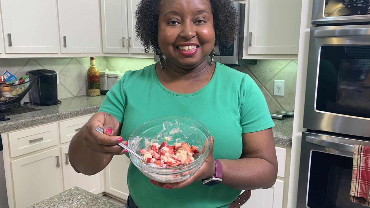 A woman holds a bowl of berries and banana cream.