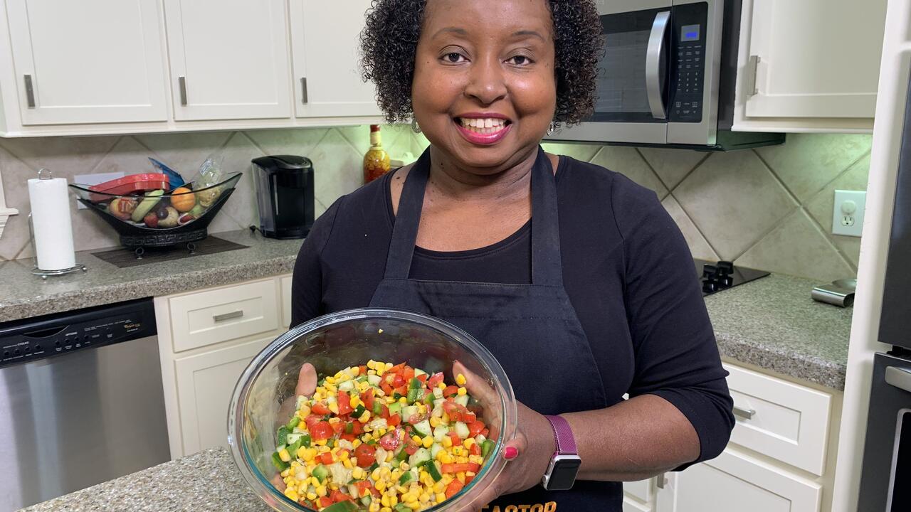 A woman holds a bowl of corn and cucumber salad.