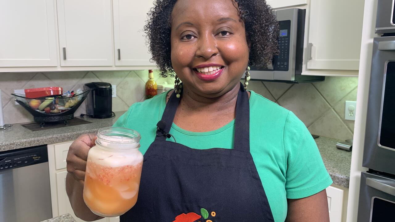 A woman in a kitchen holds a glass of strawberry pineapple lemonade.