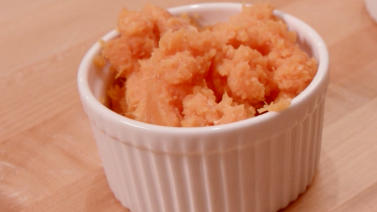 Mashed sweet potatoes in a white ceramic ramekin on a butcher block table.