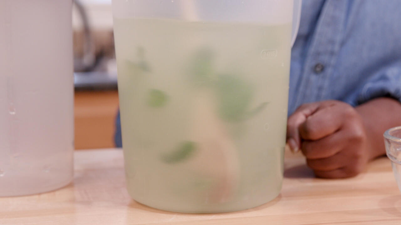 A wooden spoon is used to stir mint leaves in a pitcher of lemonad.