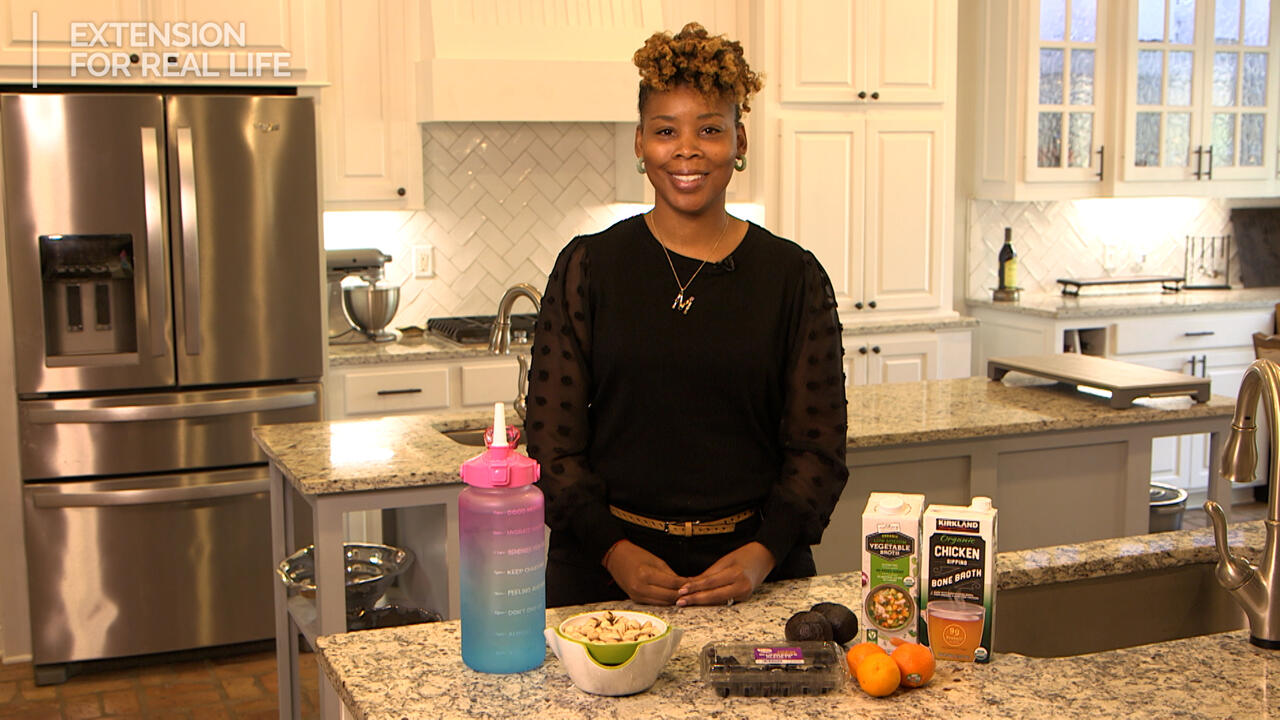 A woman stands behind a kitchen counter with food items displayed.
