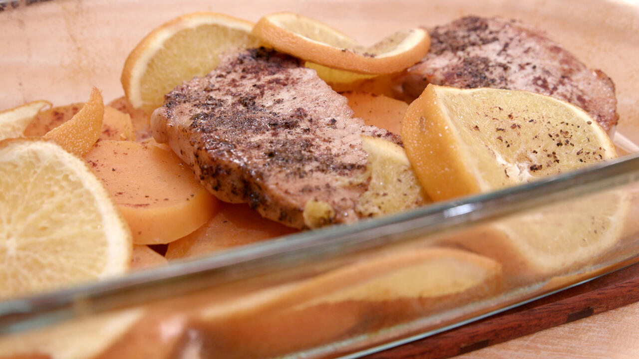 Baked boneless porkchops on sliced sweet potatoes topped with orange slices in a glass baking dish