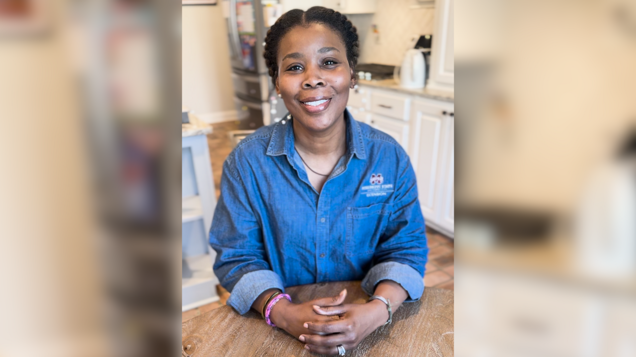 A woman sits at a kitchen table and smiles for the camera.