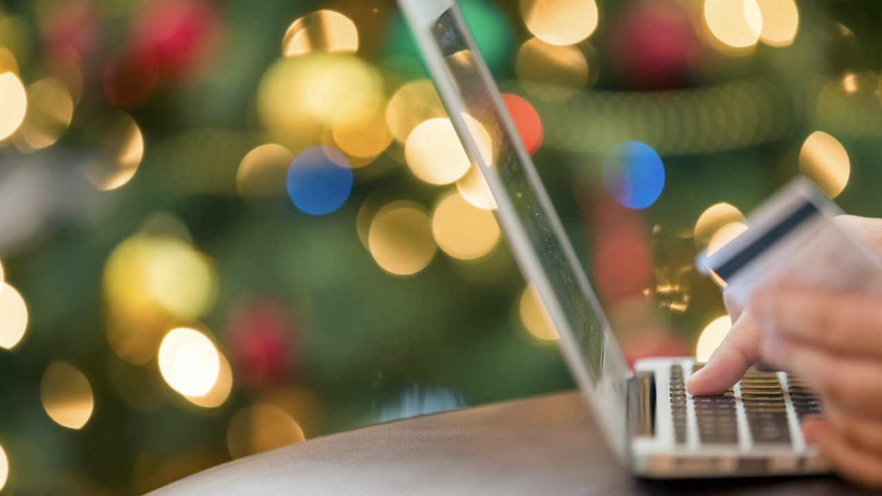 Close up view of a person ordering merchandise from a laptop computer in front of a Christmas tree.