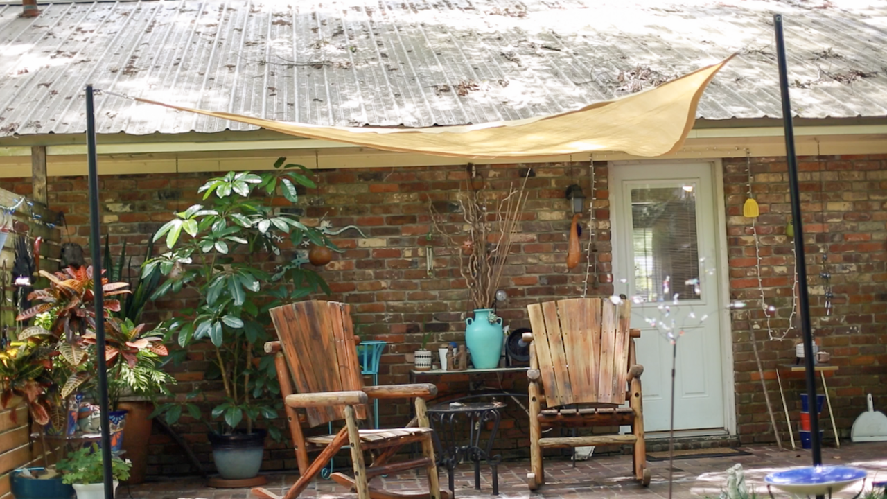 Two wooden chairs on a porch underneath a tan shade sail. 