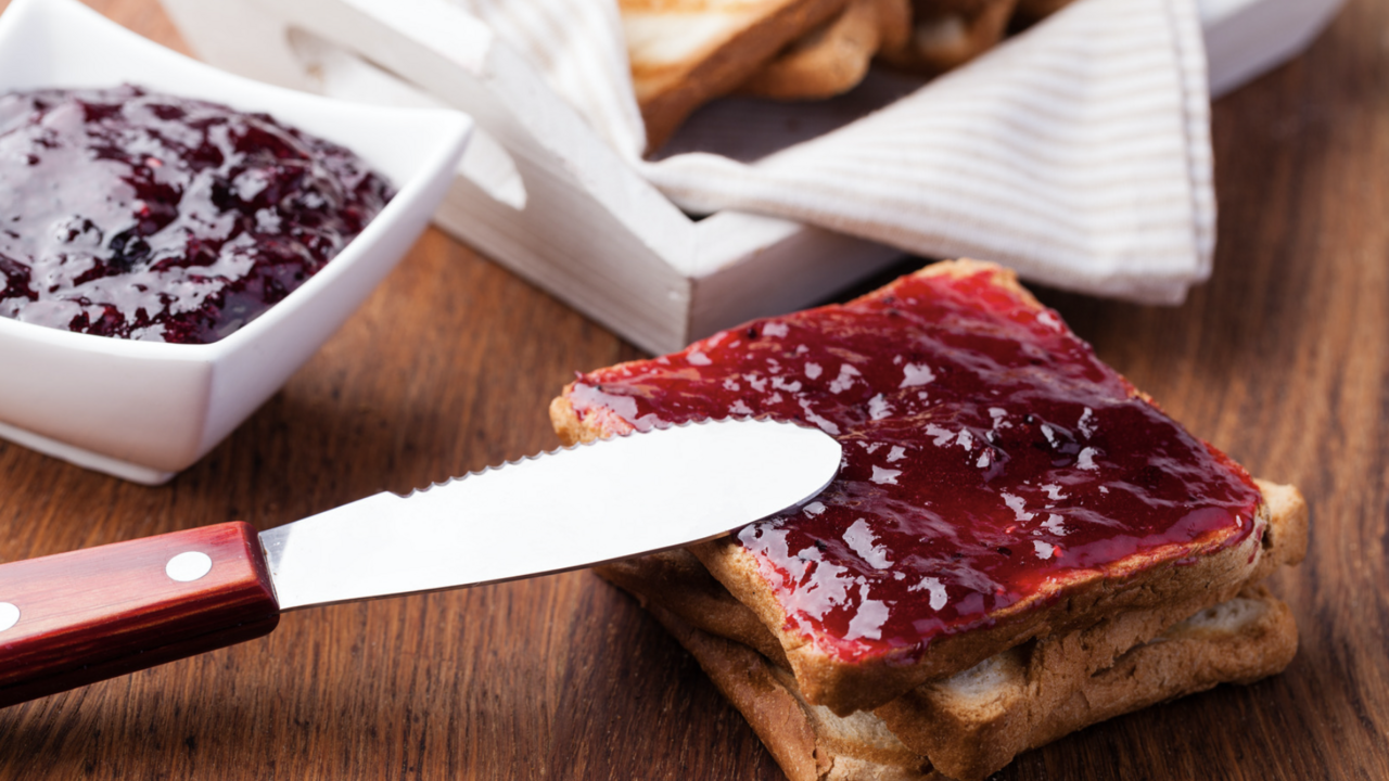 A knife spreading strawberry jam on toast.