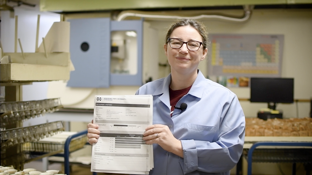 Woman in blue lab coat holding up paper.