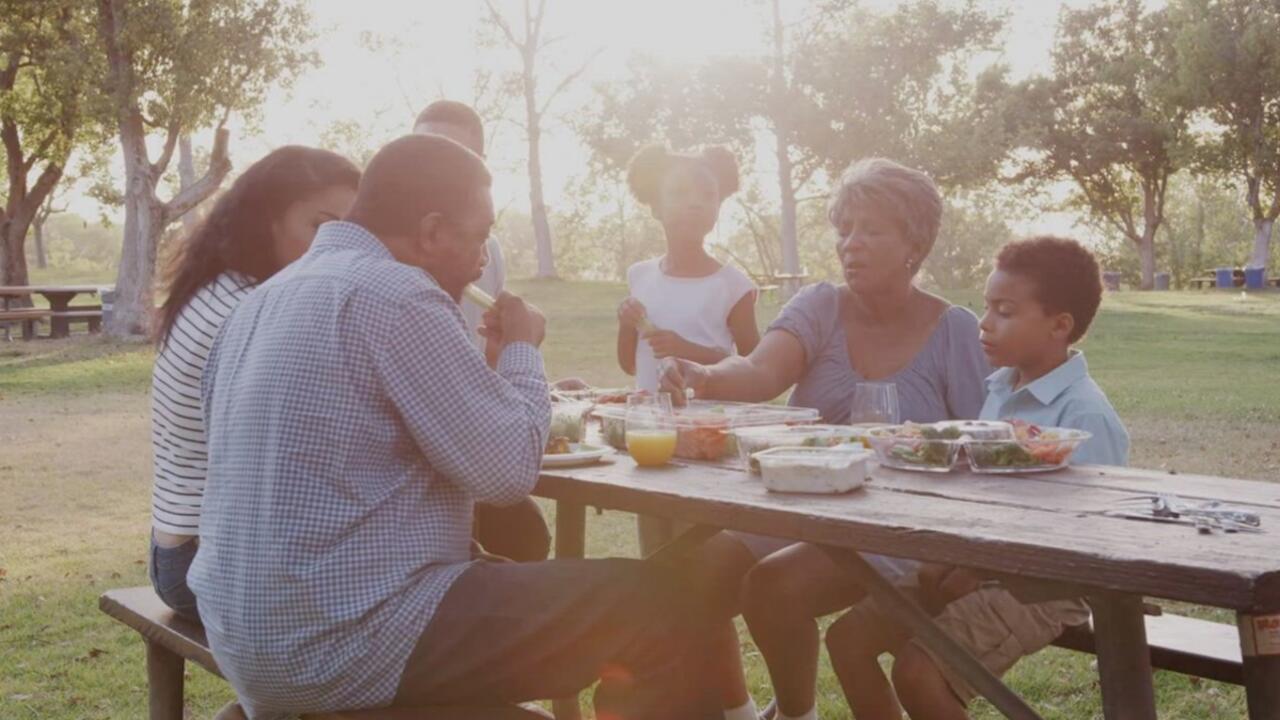 A family eats at a picnic table in the park.