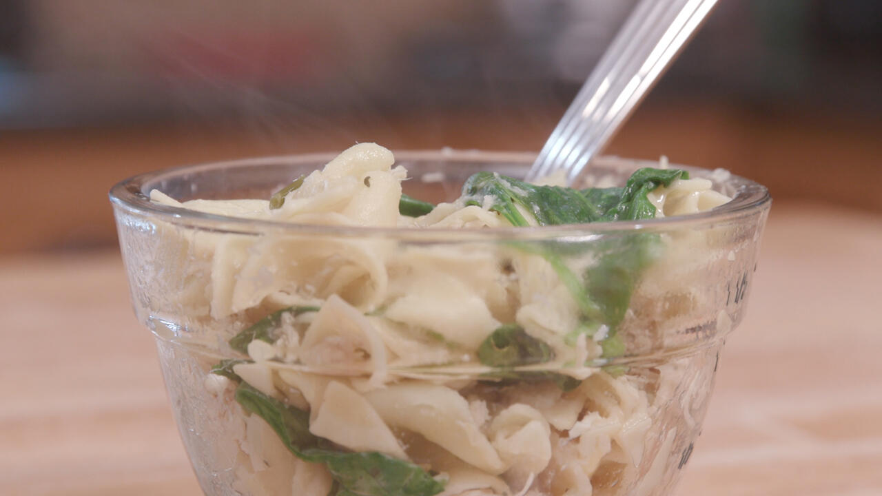 Cooked chicken, noodles, and spinach in a clear glass bowl