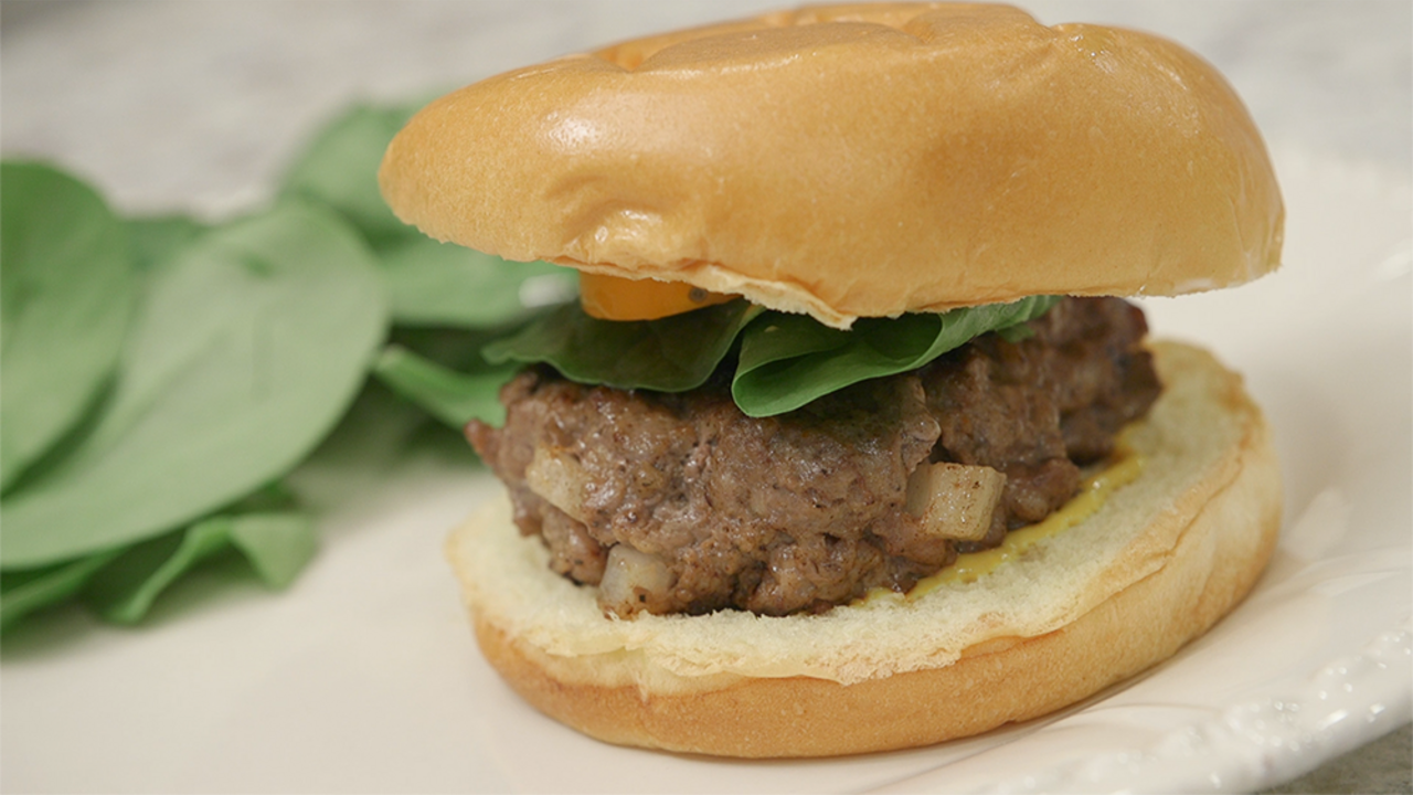 Venison burger on a bun sitting on a white plate.