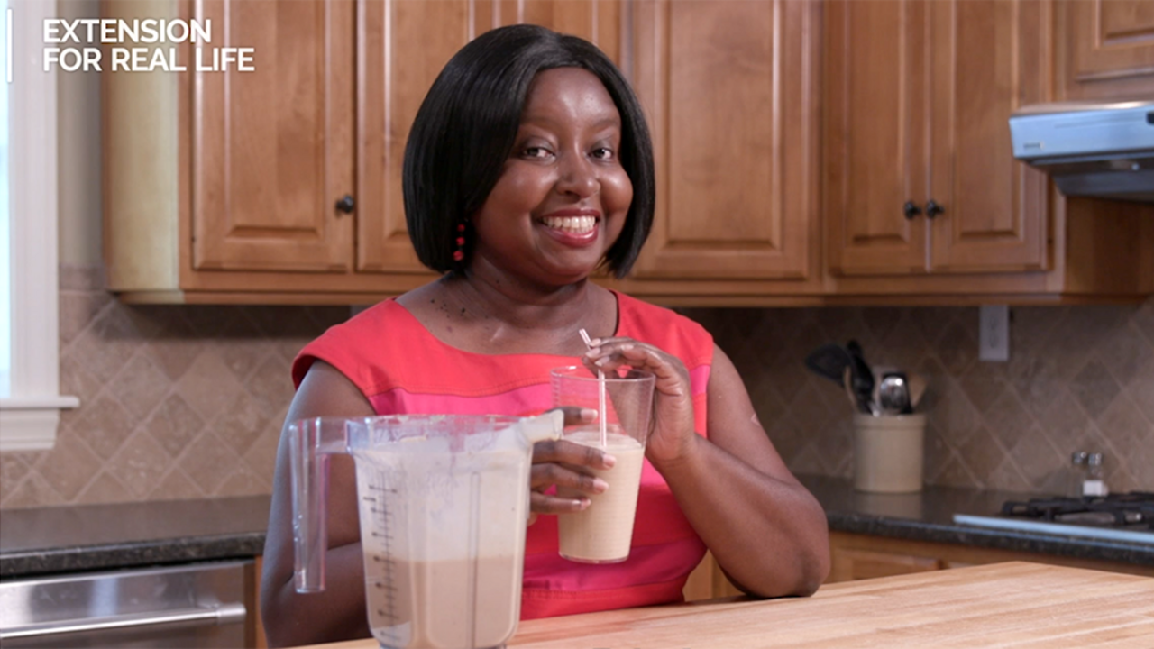 A woman holds a smoothie while standing in a kitchen.