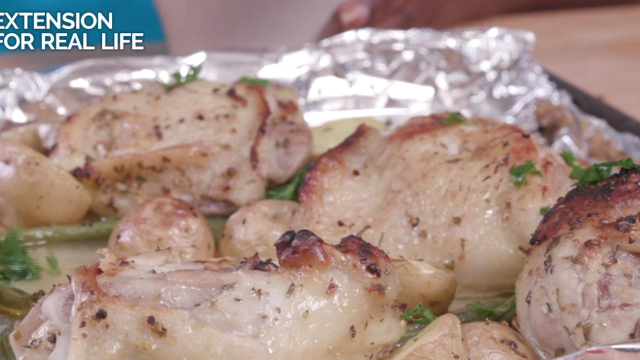 Several browned bone-in chicken thighs on top of halved baby potatoes and green beans on a foil-covered sheet pan.