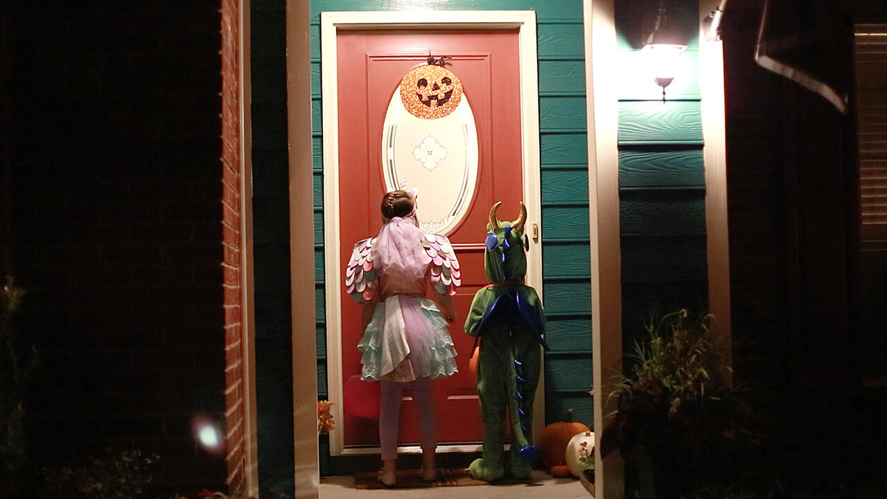 Two children waiting at a well-lit door for Halloween treats.