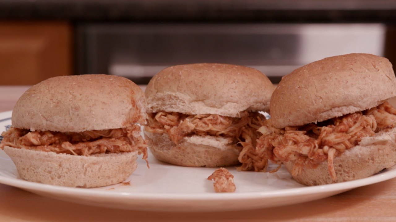 Three small sandwiches made with whole wheat slider buns, shredded chicken, and barbecue sauce on a white plate.