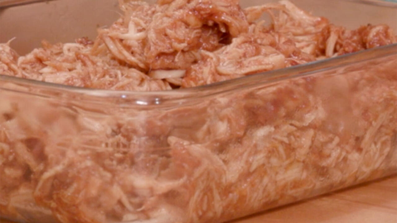 Shredded chicken breasts coated in barbecue sauce in a rectangular, clear-glass container.