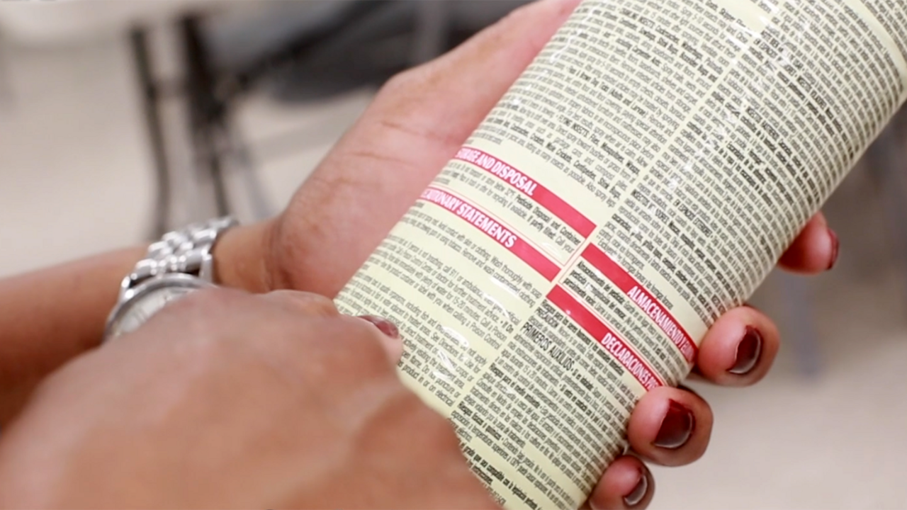 A closeup of a woman's hands holding a pesticide container while reading the instructions.