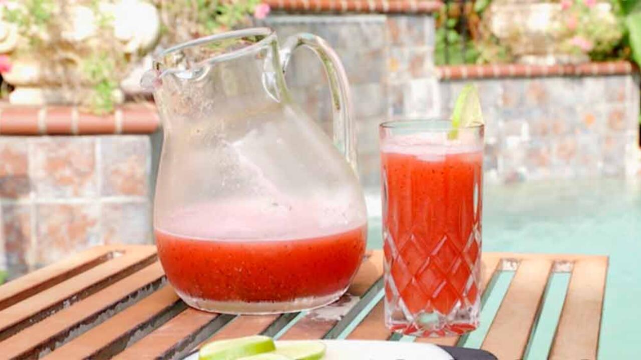 A clear glass pitcher and glass with watermelon punch.