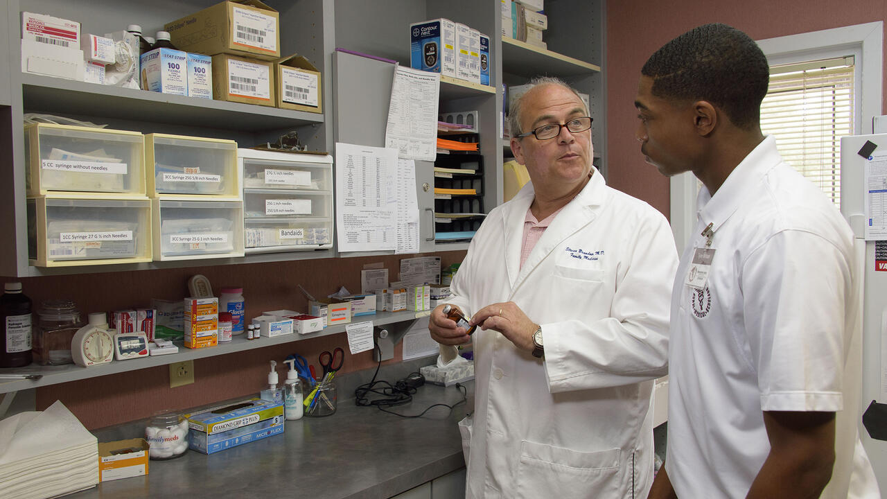 A medical doctor holds a vile of medication and talks to a young man in the Rural Medical and Science Scholars program.