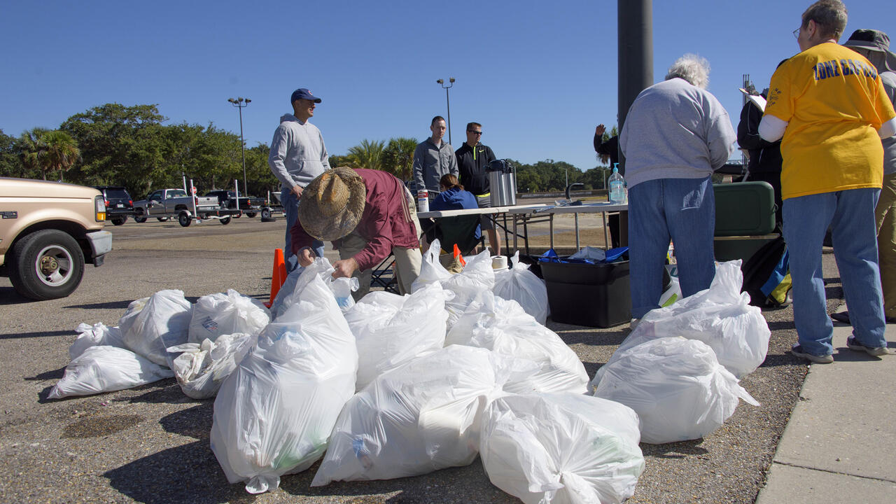 Person in straw hat tying up white trash bags.