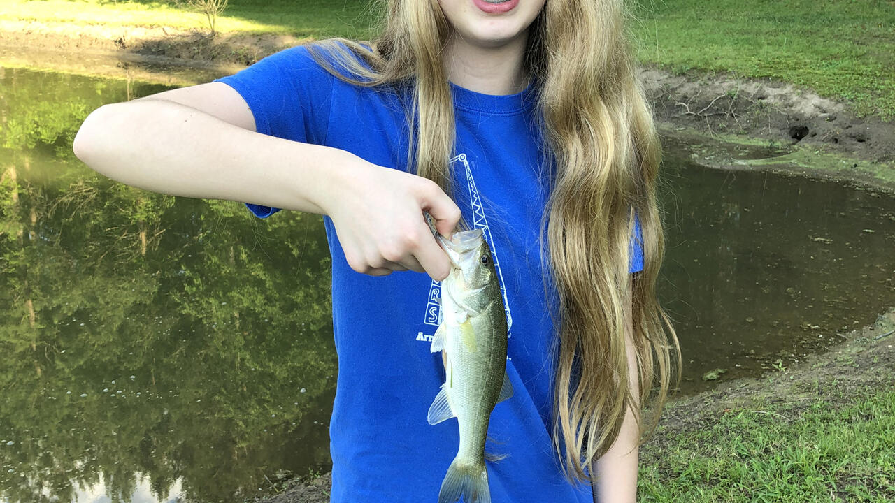 Girl in a blue T-shirt and baseball cap holding a small fish.