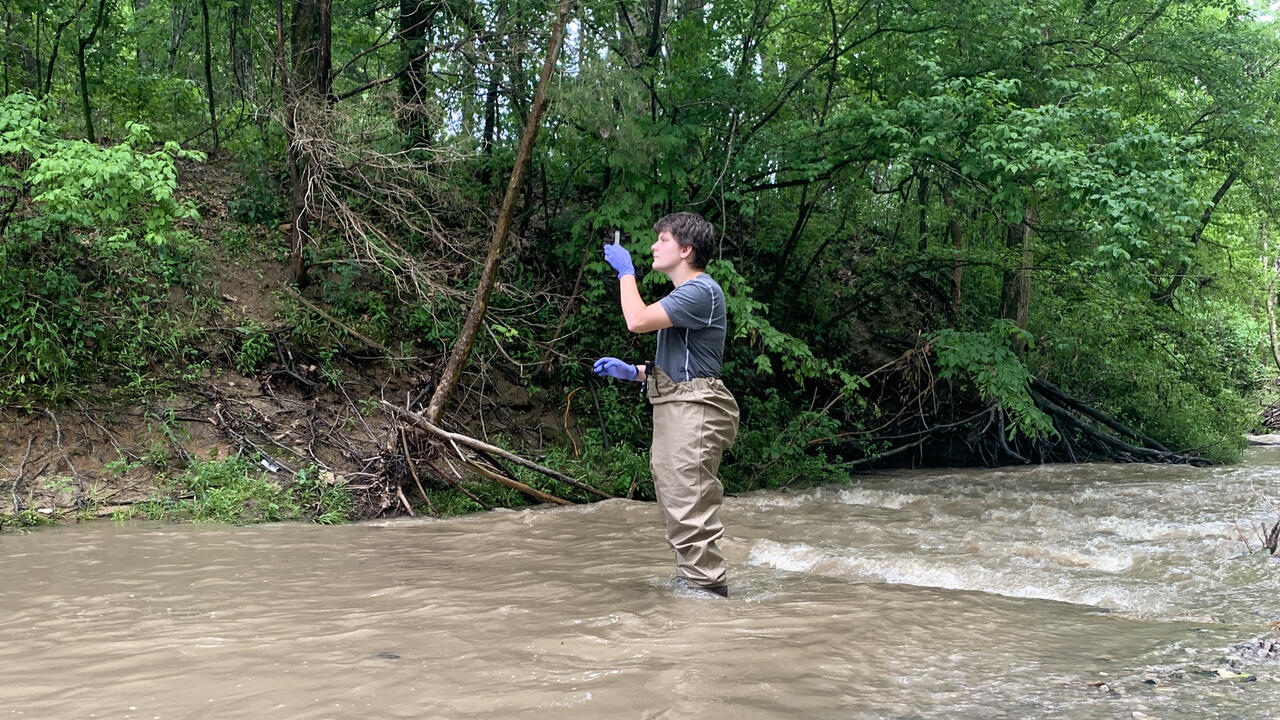 Woman in wading pants collects a water sample in a creek.