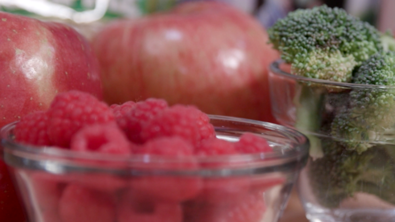 A display of produce including red raspberries in a small clear glass bowl, green broccoli florets in a small clear glass bowl, 2 red apples behind the bowls. Does that work?