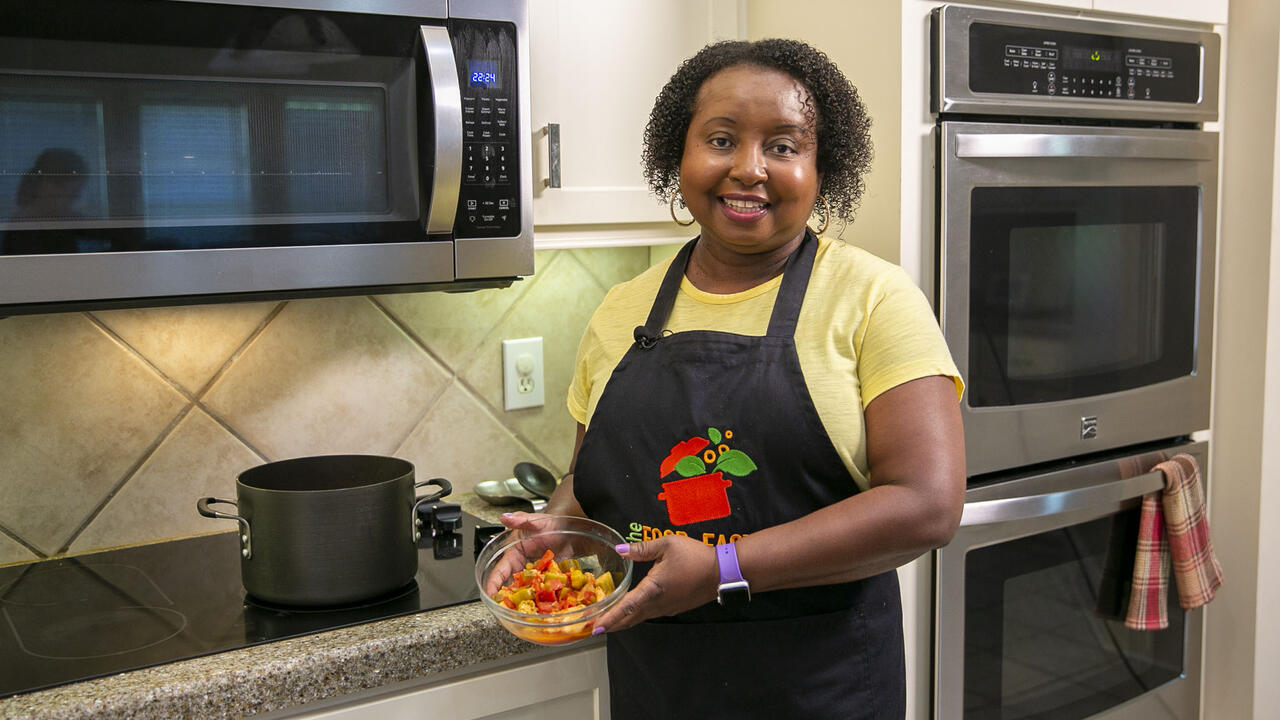 A woman stands in front of the stove with a bowl of Catfish Gumbo.