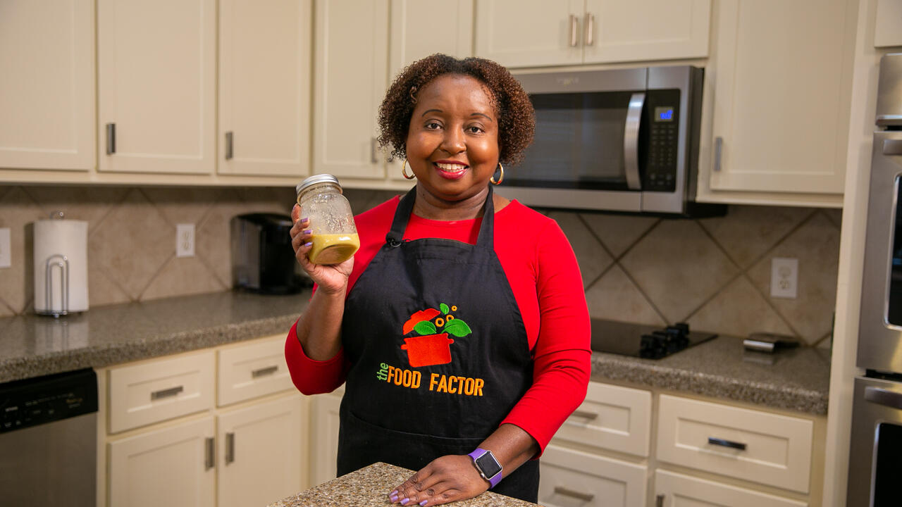 A woman holds a jar of Honey Mustard Dressing in a kitchen.