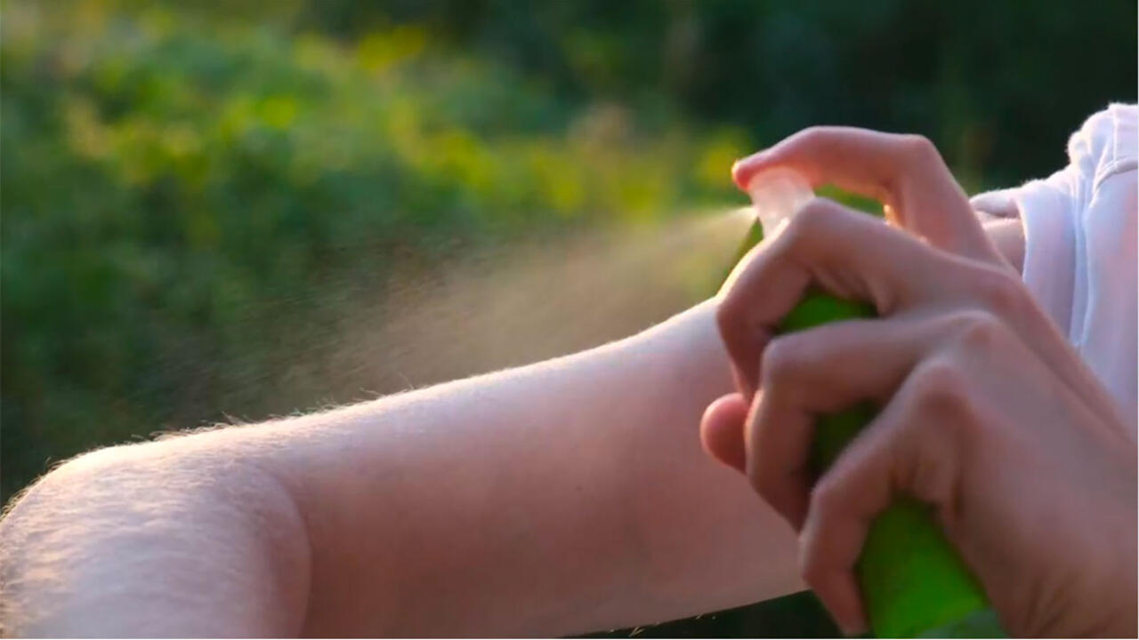 Closeup of someone spraying mosquito repellent on their arm.