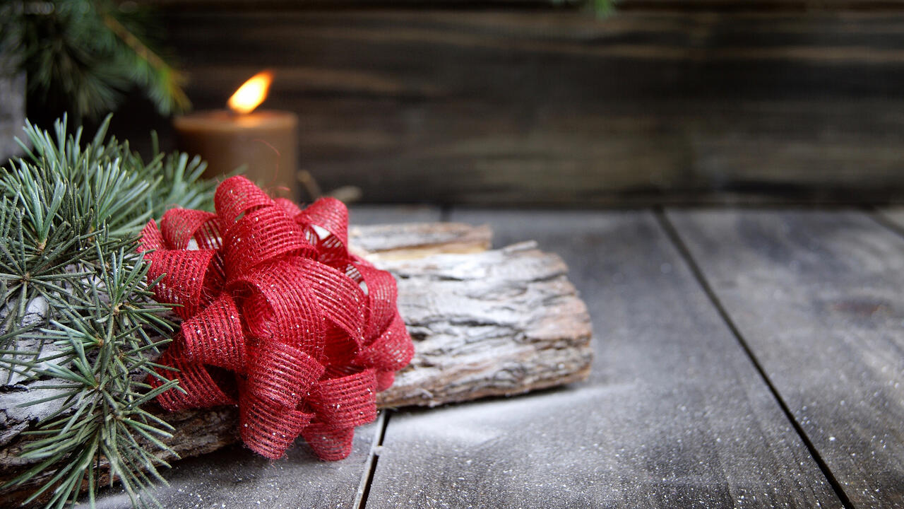 A red bow rests on a log with evergreen foliage in front of a candle.