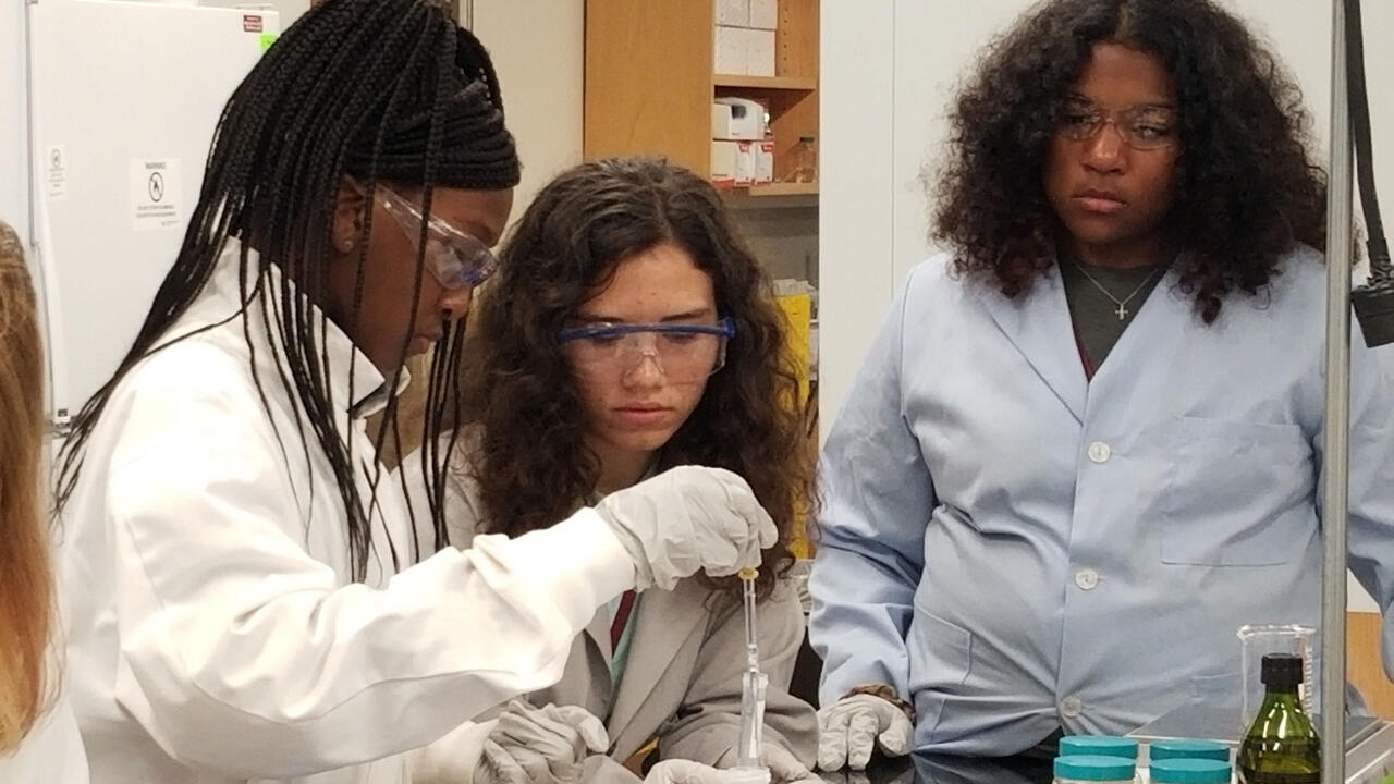 Three girls in lab coats work with scientific equipment.