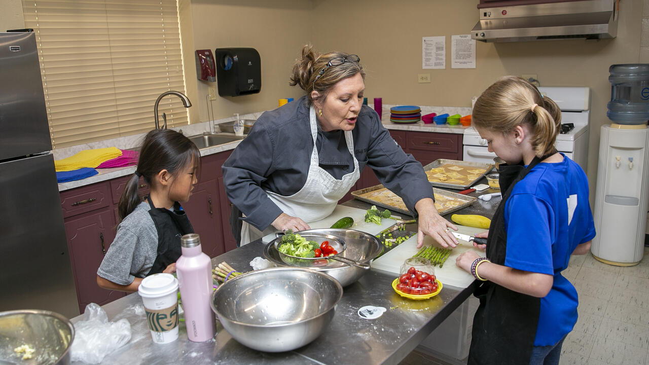  adult instructs two children in a kitchen setting.