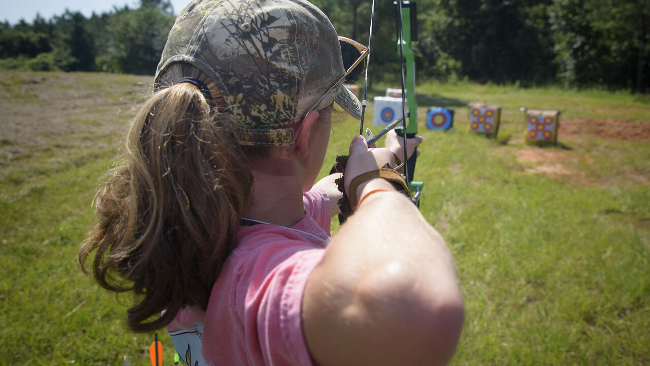 A young person pulls back a bow while aiming at a target.
