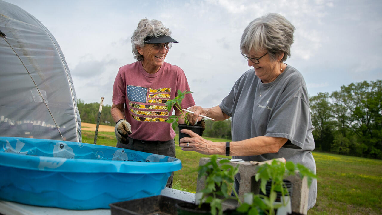 Two women work with potted plants outdoors.