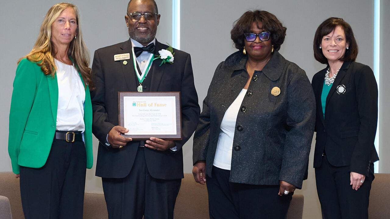 Four people stand in a line for a plaque presentation.