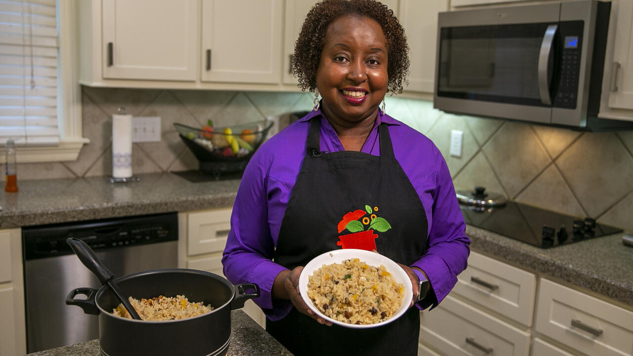 A woman stands in a kitchen with a bowl of rice pilaf posing for the camera.