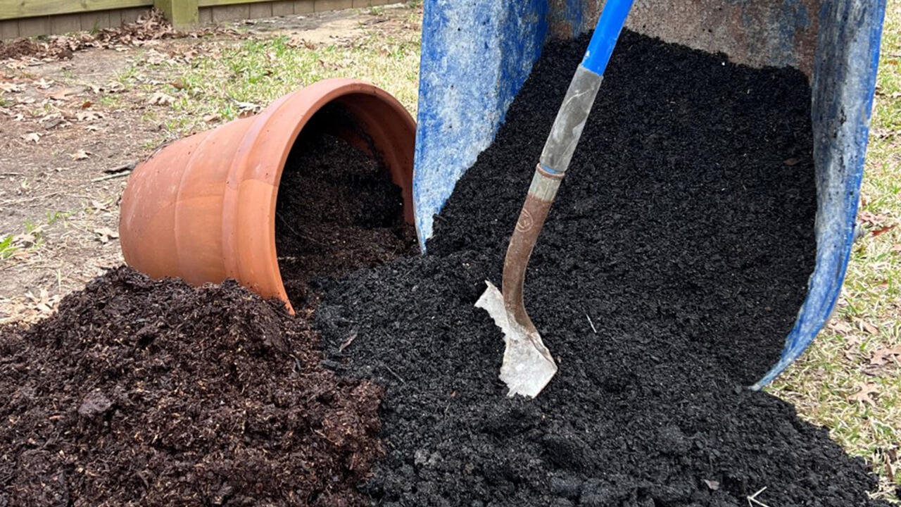 A shovel stands among soil from a wheelbarrow and a pot.