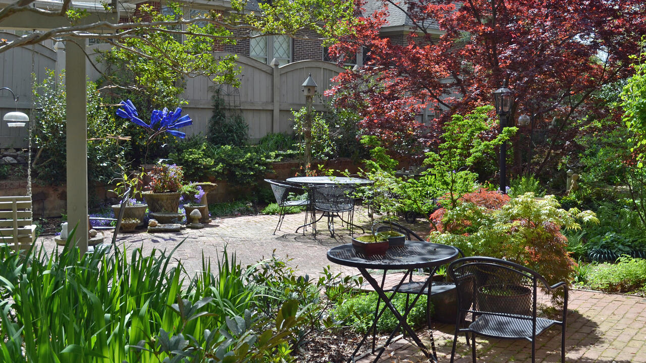 Tables and chairs are on a patio in a backyard garden.